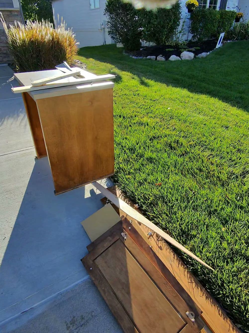 Wooden mailbox leaning on a lush green lawn, with some pieces disassembled beside it.