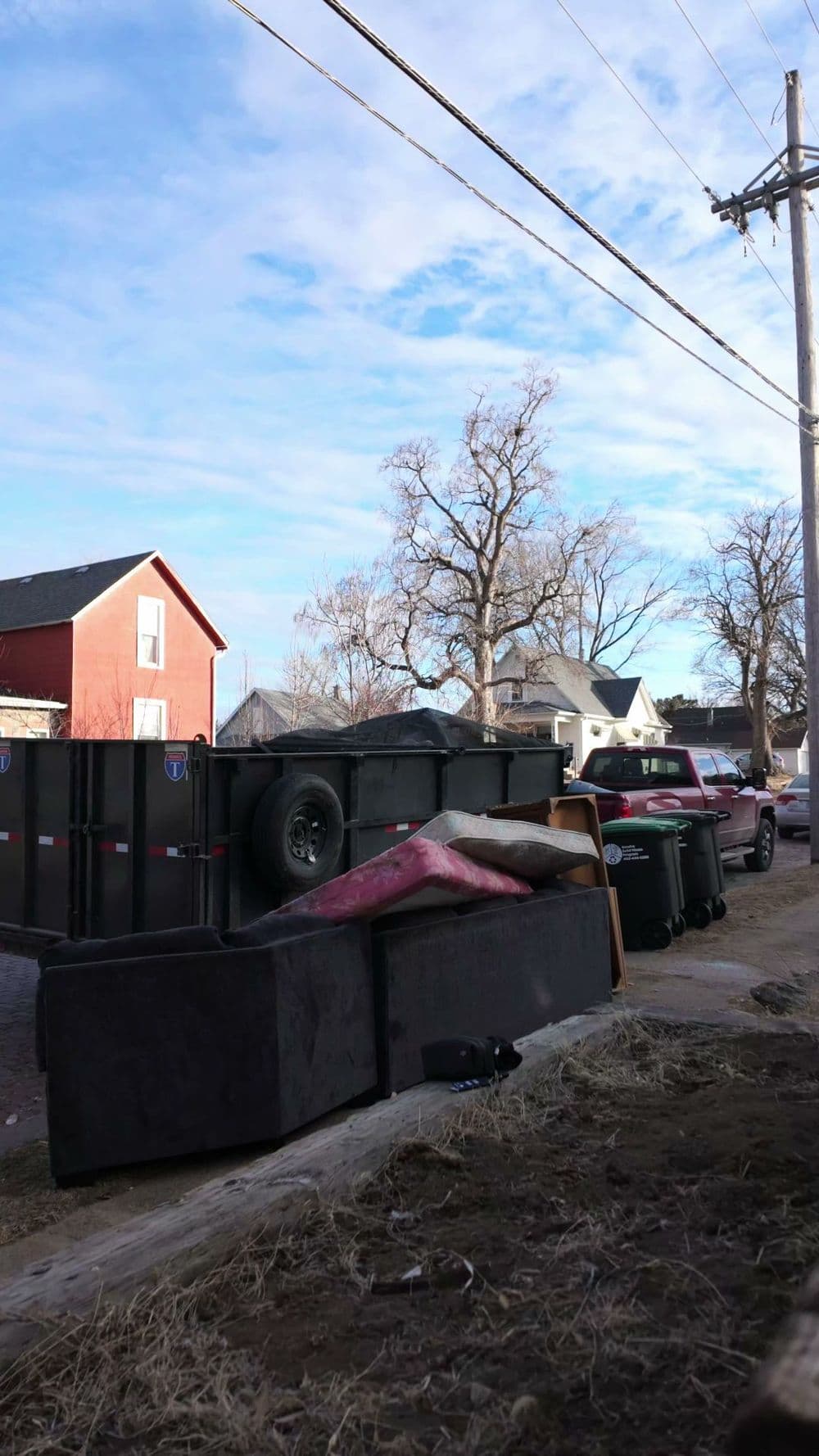 Overturned furniture and trash bins on a residential street under a blue sky.