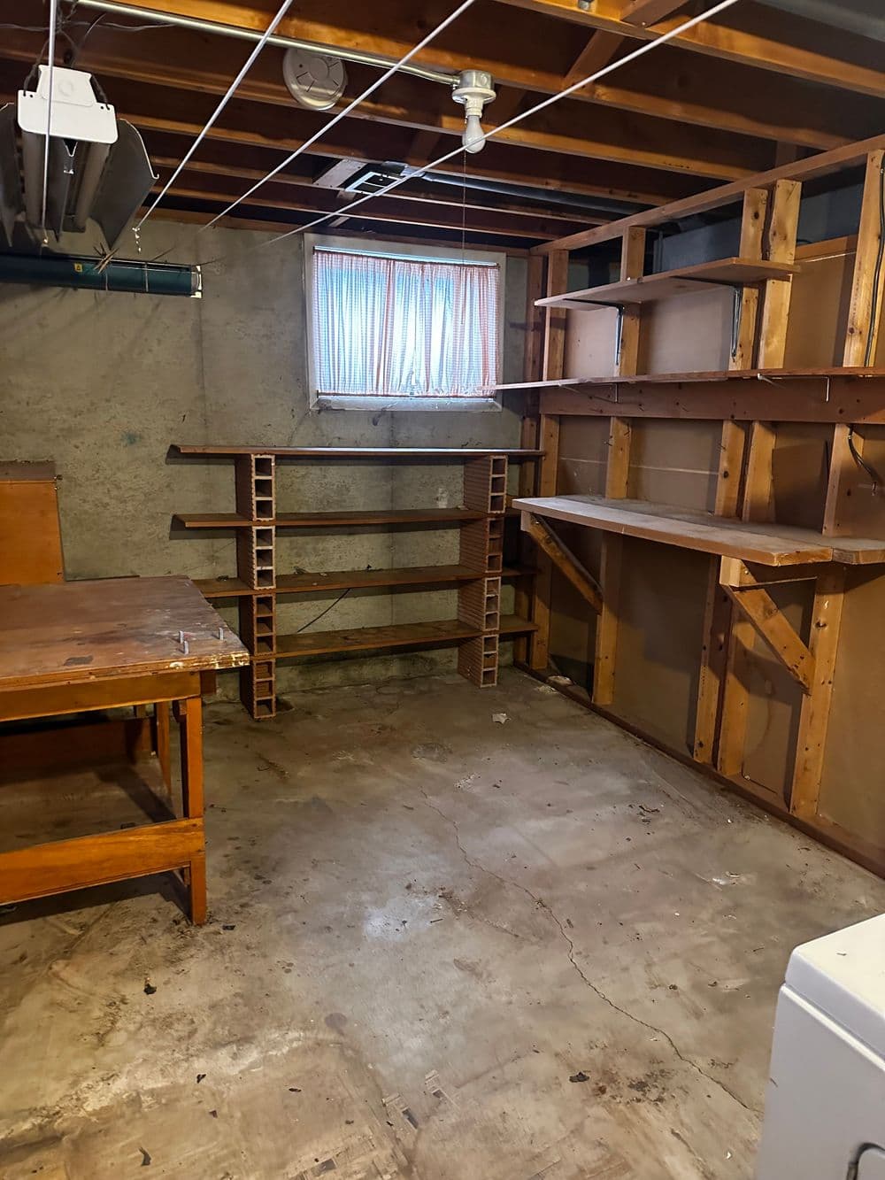 Empty basement with wooden shelves, workbench, and a small window for natural light.