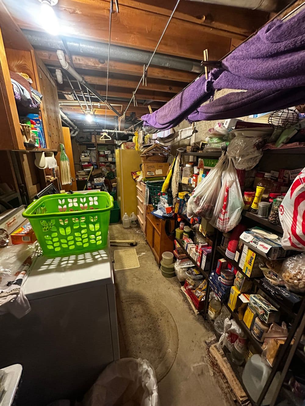 Cluttered basement storage area with shelves of food items and laundry appliances.