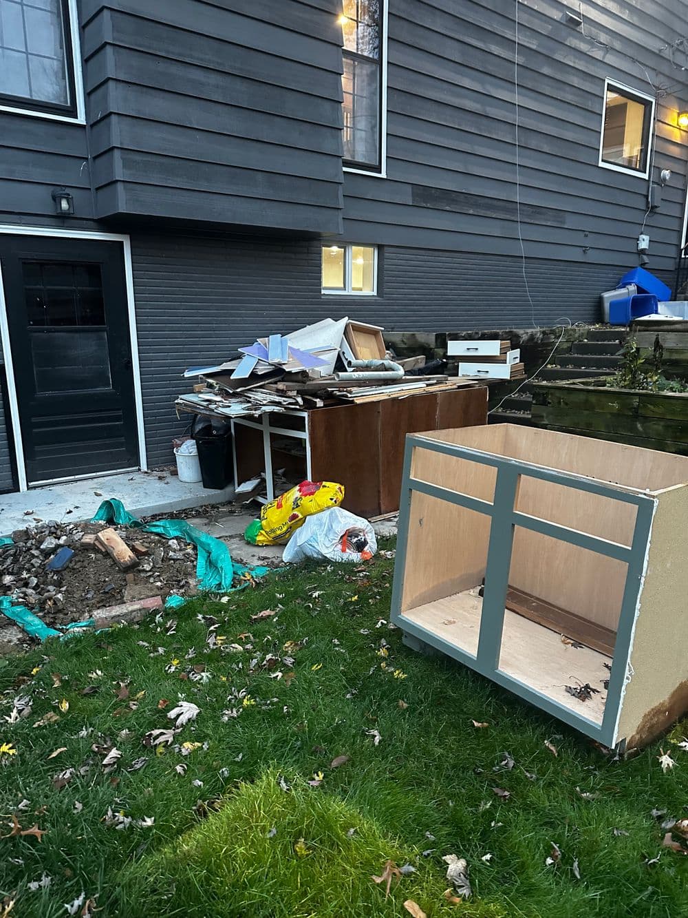 Construction debris and discarded furniture outside a house, with green trash bags in the grass.