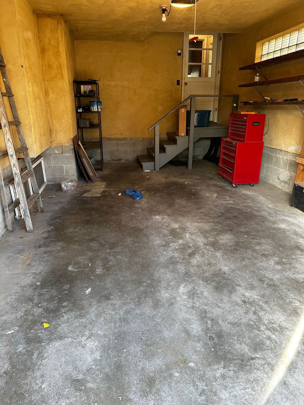 Empty garage with concrete floor, shelves, stairs, and a red toolbox.