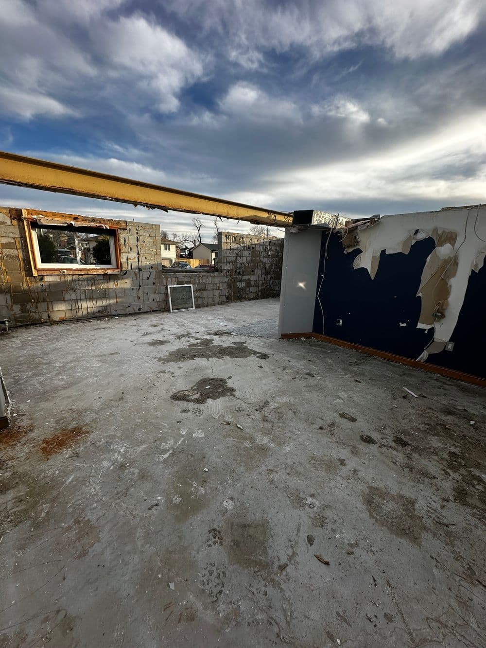 Renovation site with exposed walls, debris, and a cloudy sky overhead.