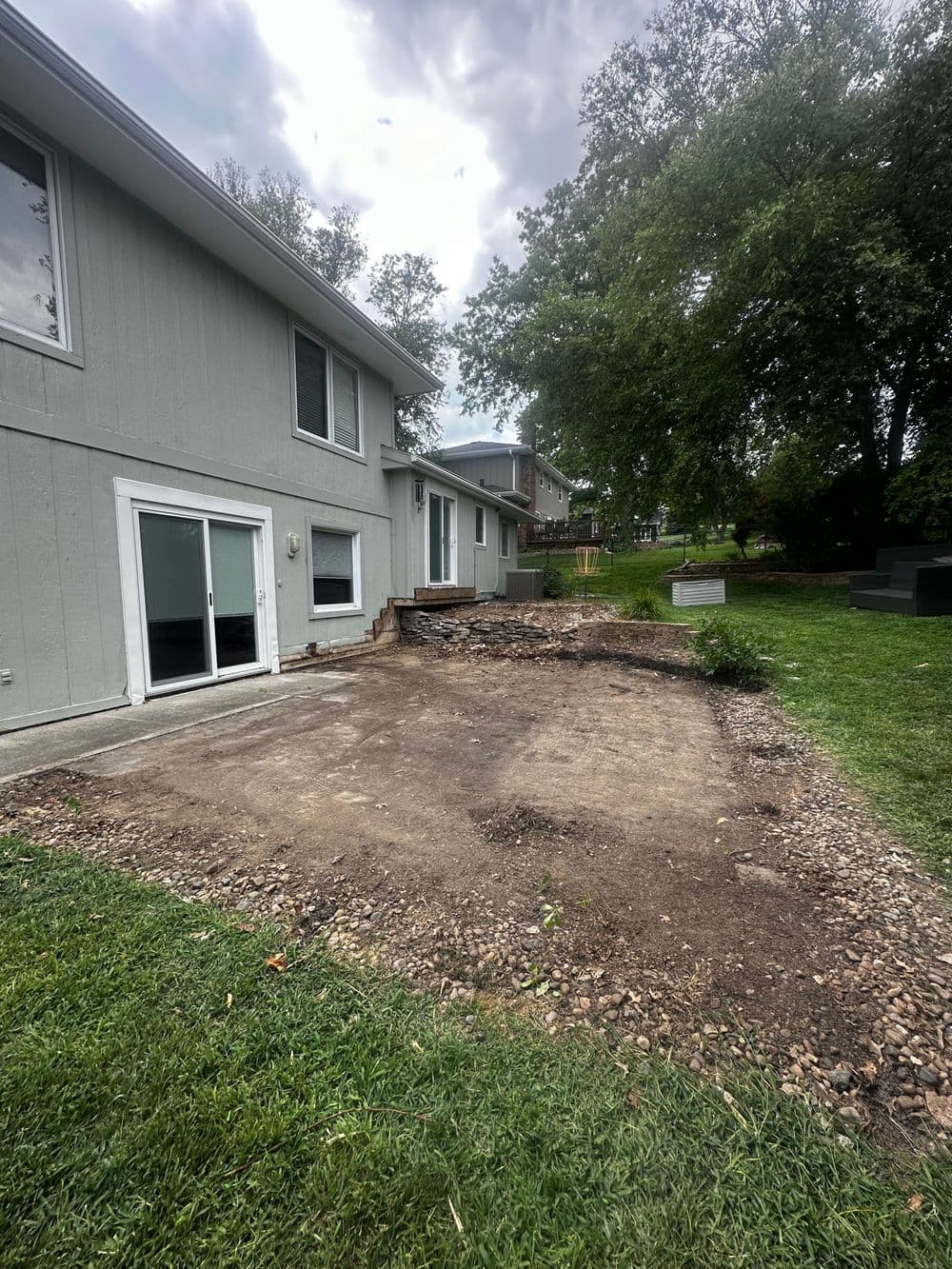Backyard renovation with cleared area and patio steps, surrounded by greenery and gray clouds.
