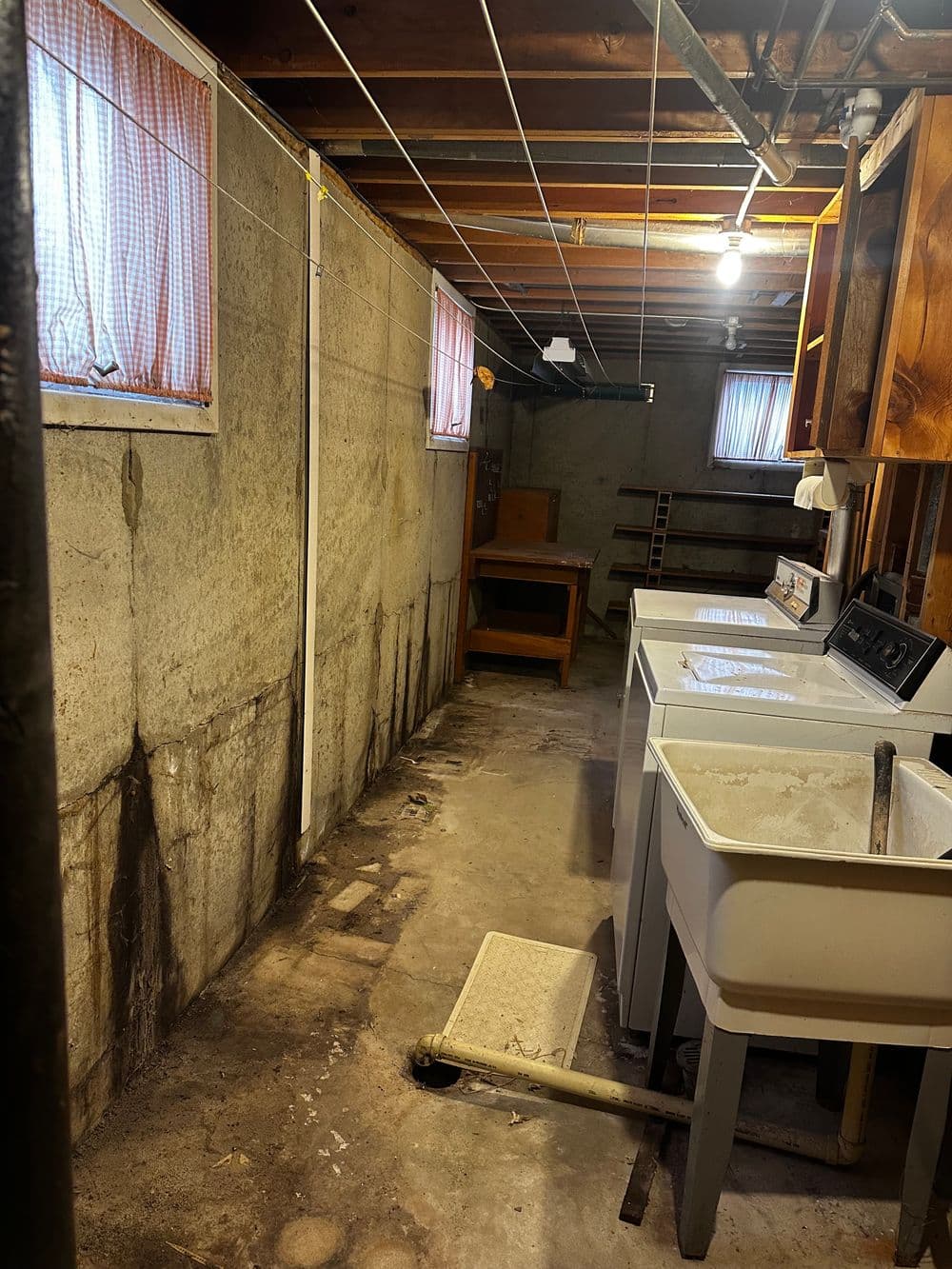 Dimly lit basement with utility sinks, exposed beams, and visible water damage on walls.