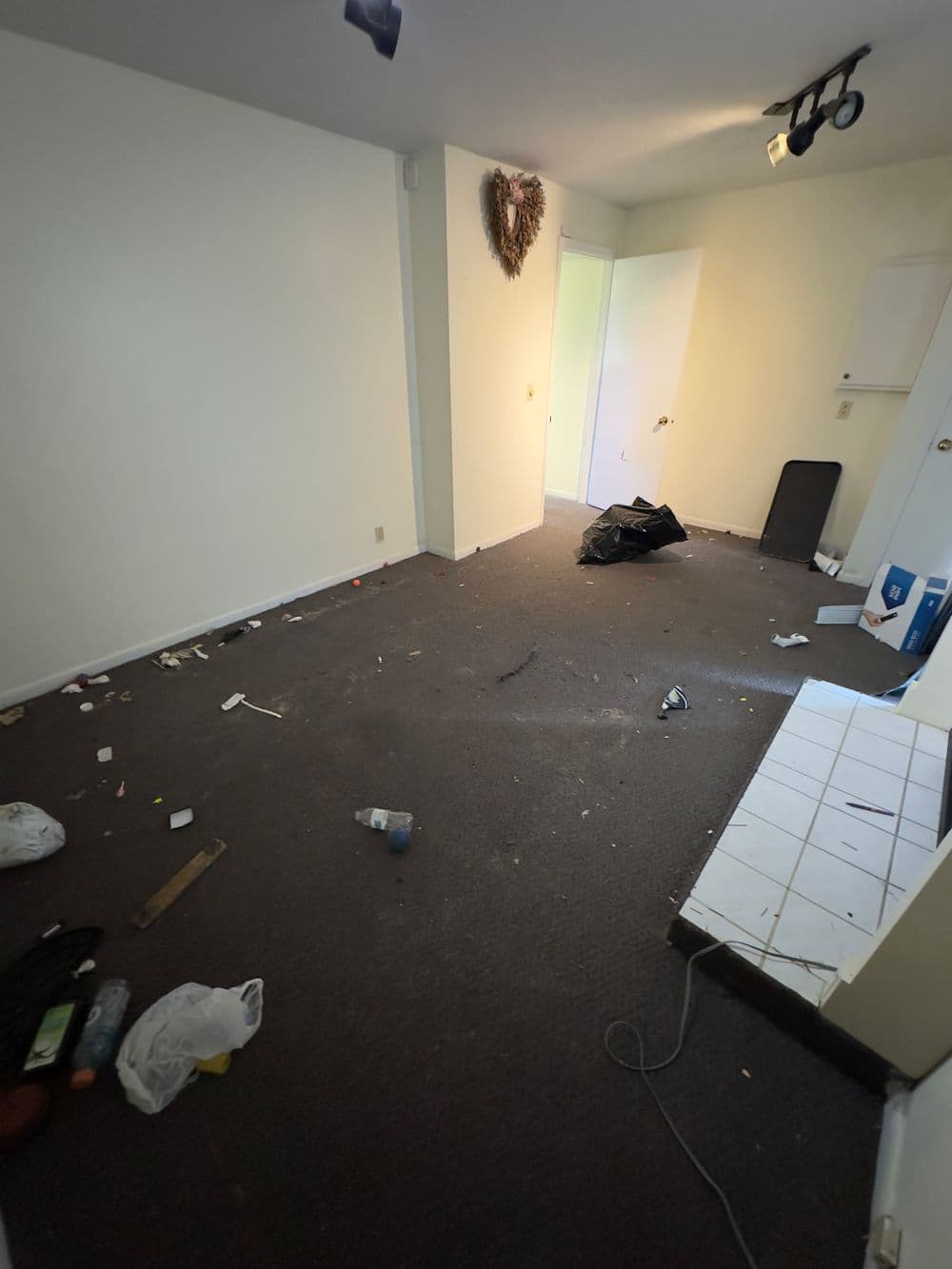 Cluttered empty room with trash and debris on the floor, unkempt walls and lighting.