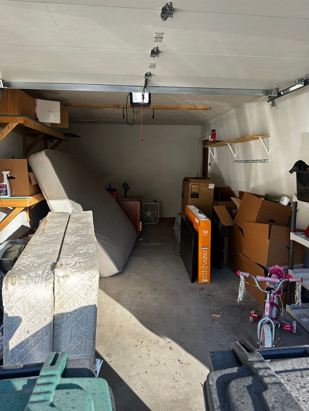 Cluttered garage interior with a mattress, boxes, and a bicycle.