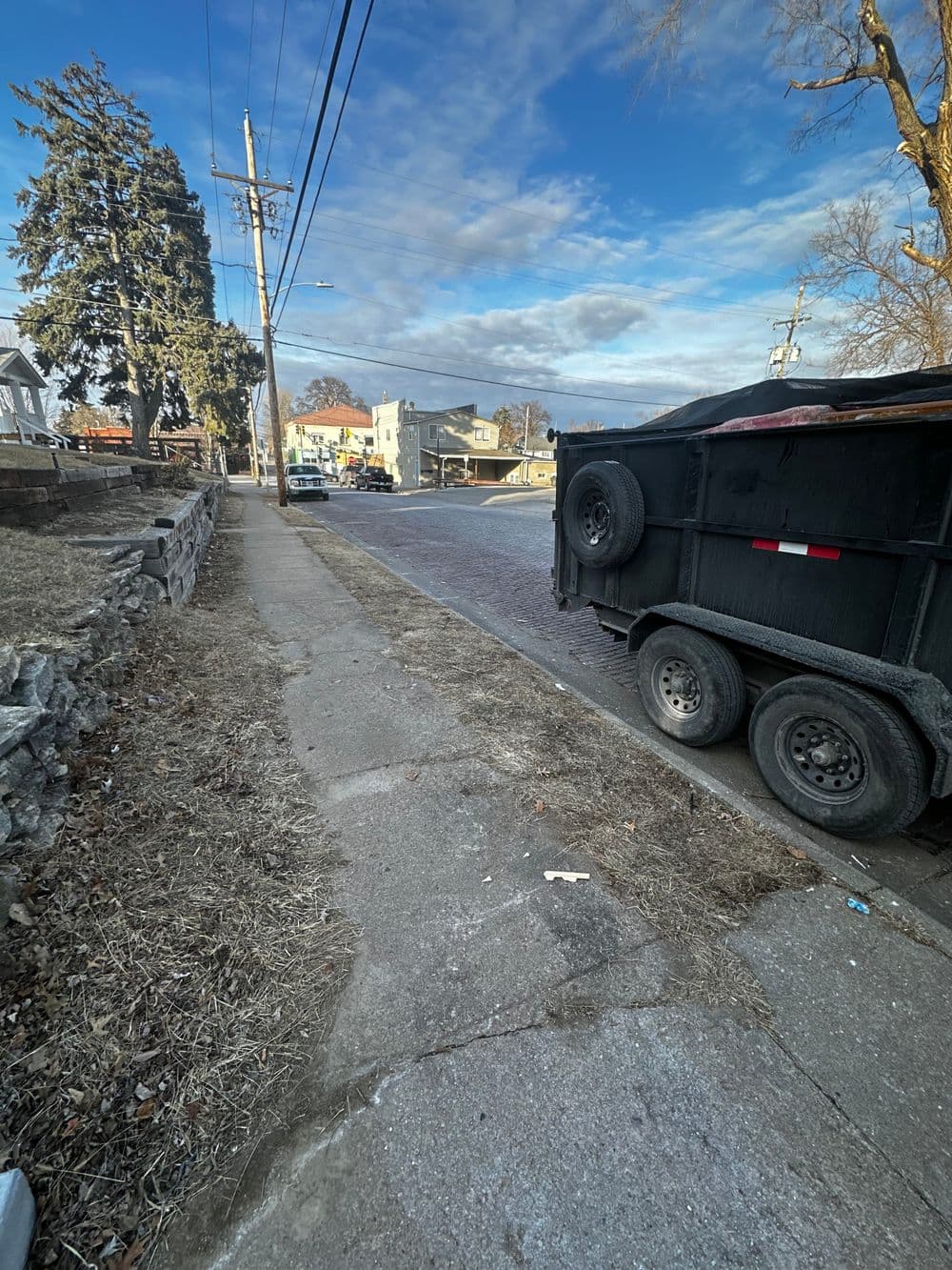 Street view featuring a utility trailer parked near a sidewalk and residential buildings.