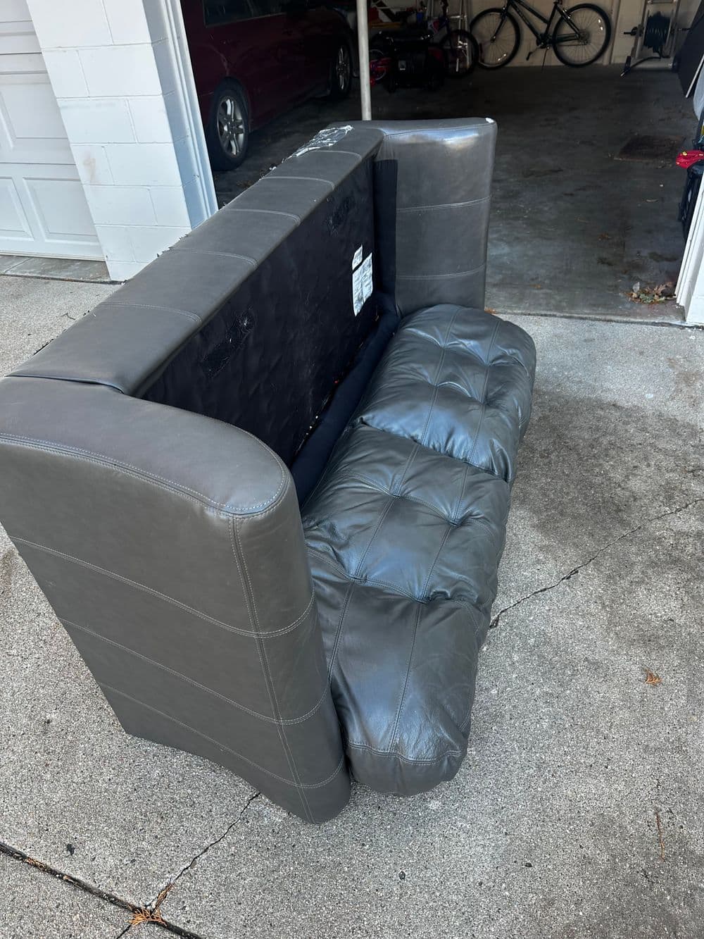 Gray tufted leather sofa positioned in a garage with a car and bicycles in the background.