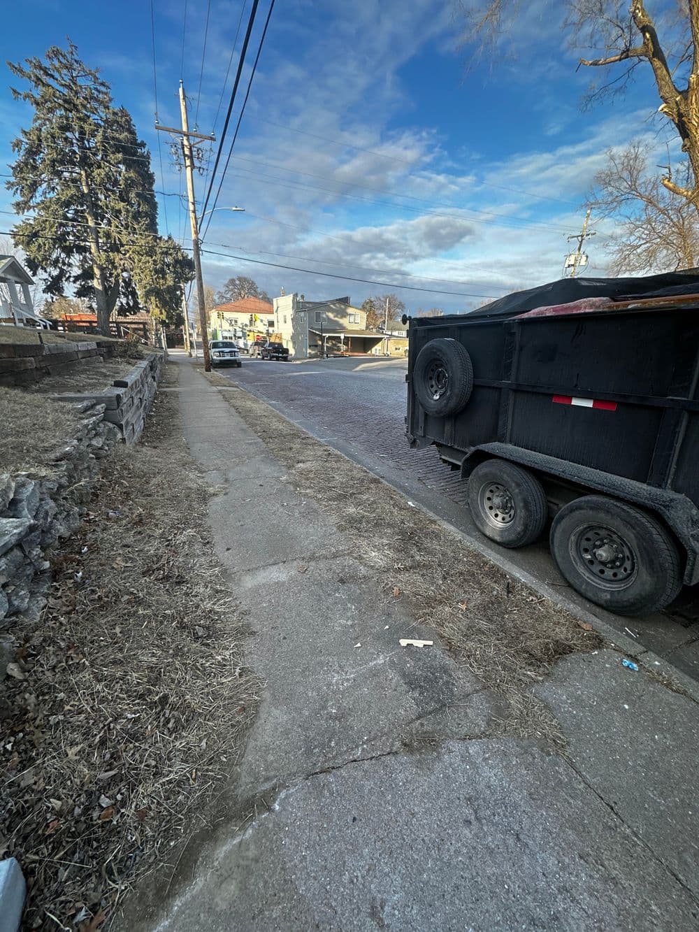 Sidewalk view of a street with parked trucks and a clear blue sky, residential area.