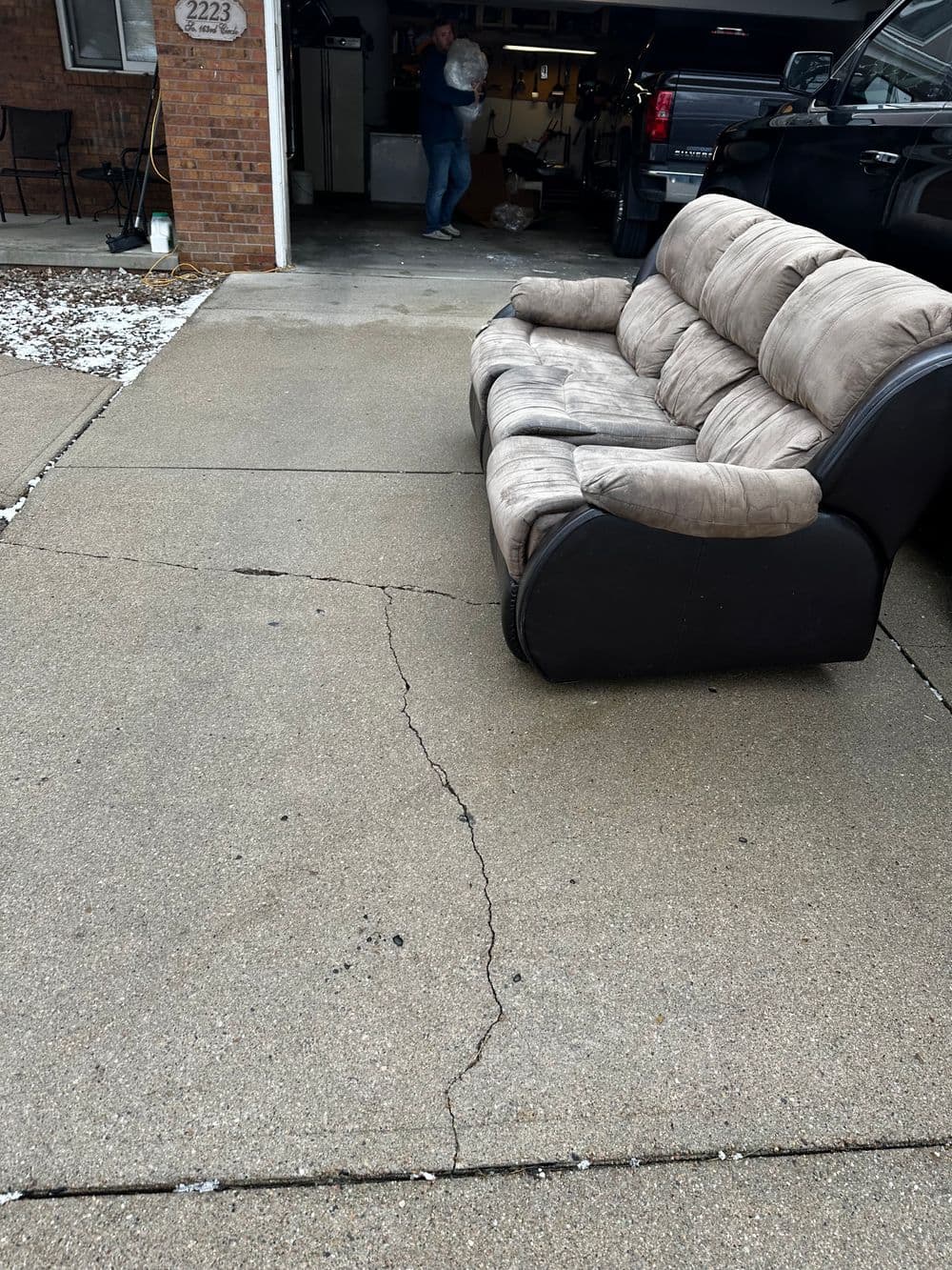 Couch on cracked driveway with a person in a garage background.