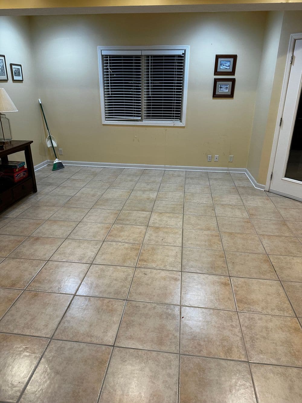 Empty room with beige tiled floor, white blinds, and framed pictures on the wall.