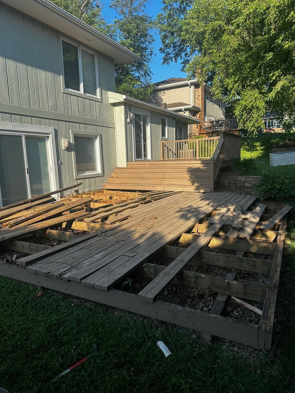 Damaged wooden deck in backyard, with exposed beams and surrounding greenery.