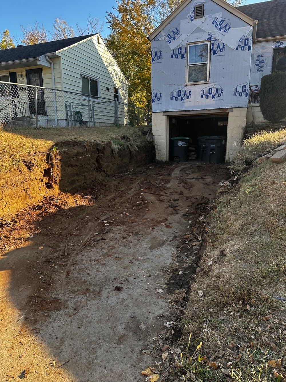 Excavated driveway area with exposed soil and trash bins near a house under renovation.