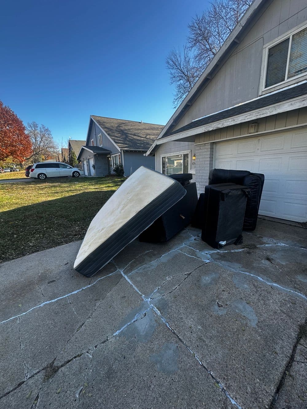 Mattresses piled outside a house on a driveway with clear skies and trees in the background.