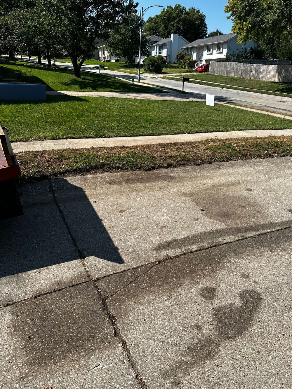 Street view showing a clean concrete driveway with a grass lawn and residential houses in background.