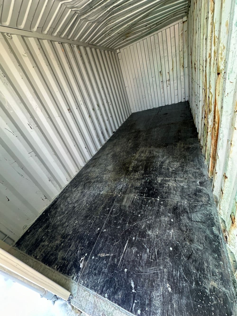 Empty metal storage container interior with worn flooring and rusted walls.