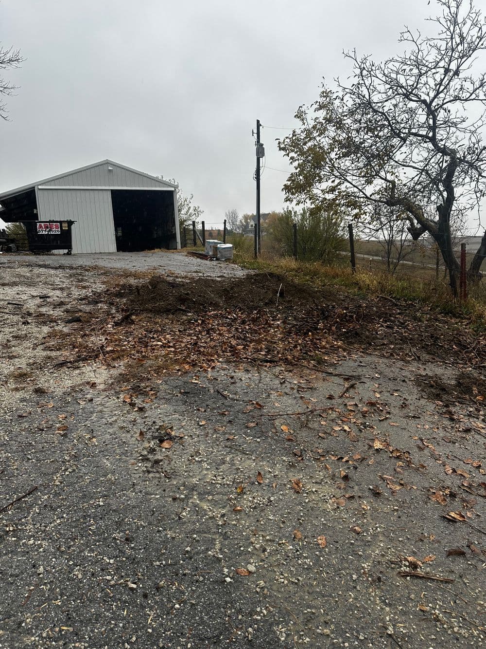 Gravel driveway with mud and leaves near a storage shed on a rainy day.