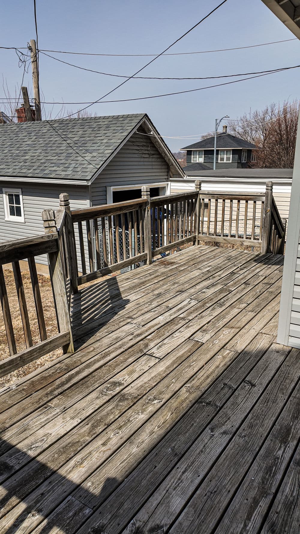 Wooden deck with railings, overlooking a neighborhood, under clear blue sky.