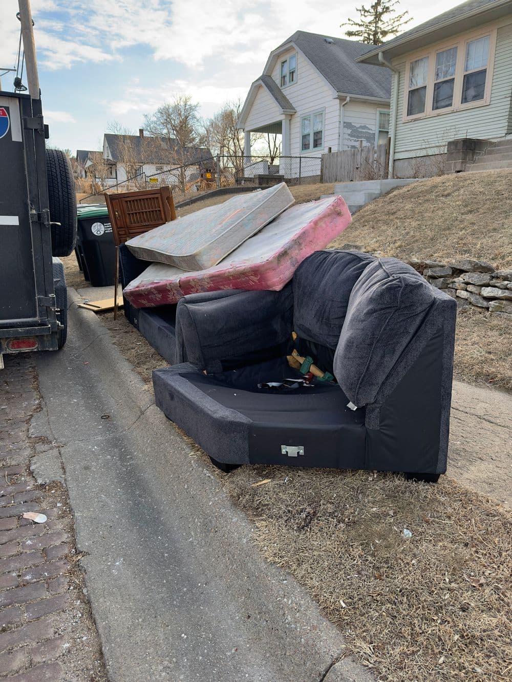 Abandoned couch and mattresses on a curbside near residential homes.
